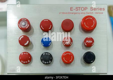 A display panel showcasing various red, black, and blue 16mm emergency stop switches and push buttons for industrial machinery safety and control syst Stock Photo