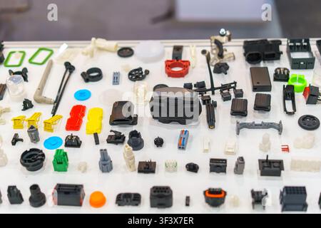 High-angle view of various colorful plastic injection molded components, electronic connectors, and automotive parts displayed on a white table. Stock Photo