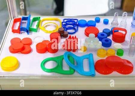 Close-up of various colorful plastic bottle caps, lids, and carrying handles arranged on a white table at a packaging manufacturing exhibition. Stock Photo