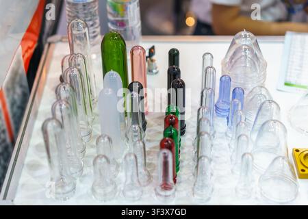 Close-up of various sizes and colors of PET plastic bottle preforms arranged on a white table at a manufacturing exhibition. Stock Photo