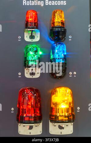 Illuminated industrial rotating warning beacons in red, yellow, green, and blue mounted on a display panel, used for factory safety, emergency signals Stock Photo