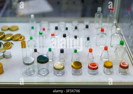 A diverse collection of small, empty glass bottles and cosmetic jars with colorful caps arranged on a white display table, showcasing various packagin Stock Photo
