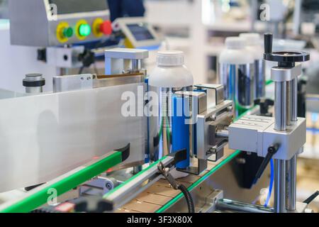 Close-up of an automatic labeling machine applying white paper labels to plastic bottles moving along a conveyor belt in a modern manufacturing plant. Stock Photo