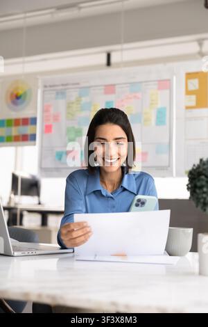 Businesswoman reviewing report and checking phone in office Stock Photo