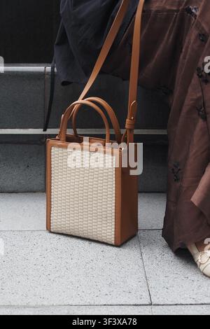 Small handbag sits on a floor near a person's leg Stock Photo