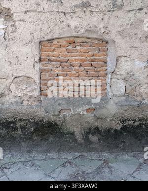 Old building's exterior showcasing a rough brick infill within crumbling gray plaster, creating a grungy urban pattern with visible cracks and decay a Stock Photo