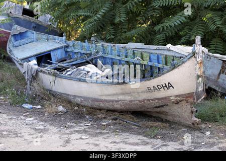 Old wooden fishing boat from varna, bulgaria, showing clear signs of abandonment and decay, sitting on dry land with peeling paint and debris, conveyi Stock Photo