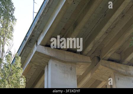 Concrete highway bridge structure captured from a low angle, showing visible beams, supports, and the robust construction of urban infrastructure agai Stock Photo