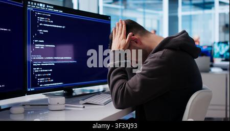 Young Software Engineer Looks Tired And Stressed While Coding At Desk. Stock Photo
