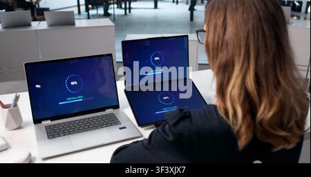 Woman Using Laptop To Install New Software Update On Touchscreen Device. Stock Photo