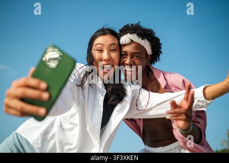 Trendy digital creator couple taking selfie by the beach, sharing travel content for social media Stock Photo