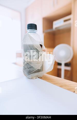 Plastic bottle wrapped in crumpled paper on wooden desk in modern Japanese home office, soft Stock Photo