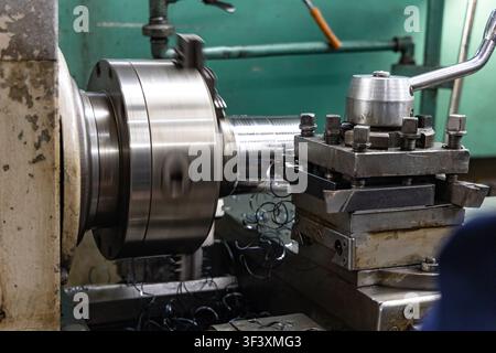 Industrial lathe machining steel shaft in metalworking manufacturing workshop Stock Photo