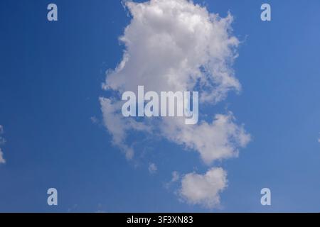 A single white fluffy cloud floating isolated in a clear blue sky on a bright sunny day. High Quality Photo Stock Photo