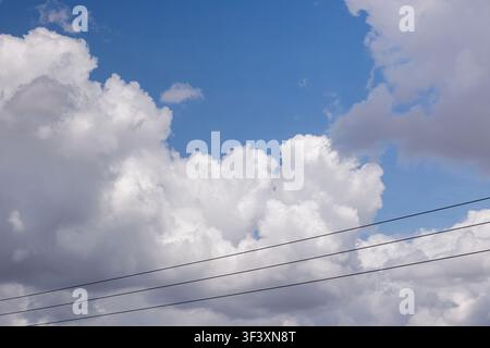 Clear blue sky filled with fluffy white cumulus clouds behind electrical power lines on a sunny summer day. High Quality Photo Stock Photo