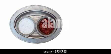 Two small bowls sit on a round silver platter. One bowl contains yogurt sauce and the other holds a red spicy dip. This is common in a restaurant. Stock Photo