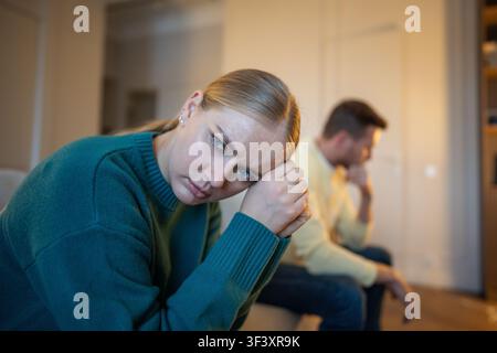 Stressed married couple sitting on couch distancing from each other after emotional family argument Stock Photo