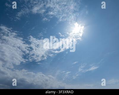 Vast blue sky filled with various clouds, from wispy to dense. Bright sun shines from the upper right, creating sunburst effects and illuminating the Stock Photo