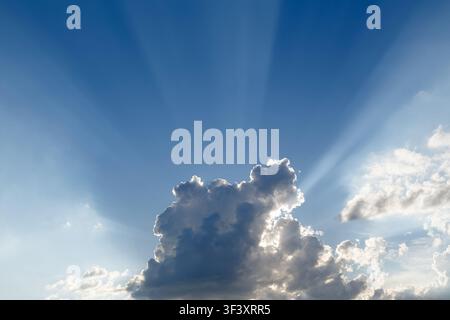 Dramatic blue sky with sun rays shining through fluffy white clouds Stock Photo