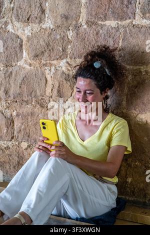 Woman smiling using mobile phone against stone wall Stock Photo
