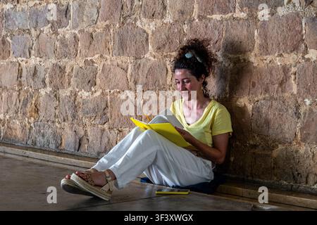 Young woman writing in notebook sitting against stone wall Stock Photo