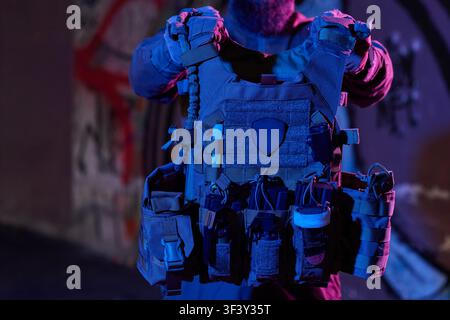 Tactical Plate Carrier Vest With Pouches and Gear Held by Operator in Urban Night Lighting Stock Photo