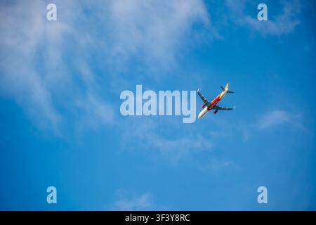 Hoi An, Vietnam, July 1, 2026. A commercial airplane with a red and white livery glides through a vibrant blue sky filled with soft wisps of white clo Stock Photo