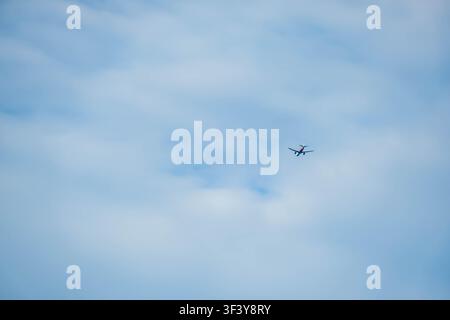 Hoi An, Vietnam, July 1, 2026. A commercial airplane with a red and white livery glides through a vibrant blue sky filled with soft wisps of white clo Stock Photo