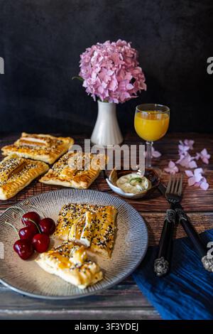 Puff pastry with Wienerli saussage wrapped with fresh cherries in the plate on the breakfast table with flowers and other decorations - dark and moody Stock Photo