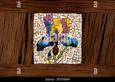Colorful glass mosaic flower artwork inset in wooden bench panel, handcrafted tile art, purple yellow blue tiles Stock Photo