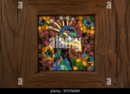 Close-up of bird head mosaic art with vivid blue green and gold tiles, rustic wooden frame, decorative craft detail Stock Photo