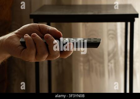 A man's hand holding a remote control for watching TV at home, on the topic of home relaxation, leisure, and TV viewing Stock Photo
