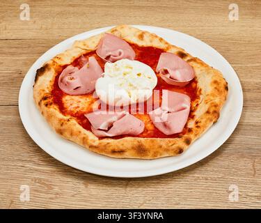 Whole Italian pizza with fresh burrata cheese, mortadella slices, and tomato sauce on white round plate on wooden tabletop. Stock Photo