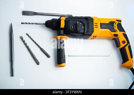 Top view of a yellow and black perforator with a handle, a set of drills, chisels and fasteners on a Stock Photo