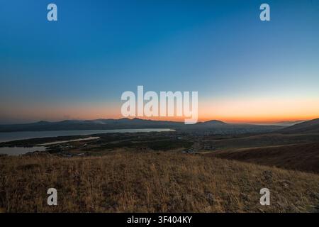 A breathtaking view over the Sevan valley at sunset, with orange skies fading into deep blue above the lake and the silhouettes of mountains in the di Stock Photo