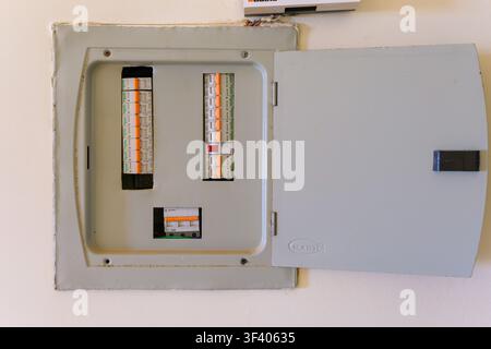 Open electrical distribution board with Schneider Electric miniature circuit breakers, showing exposed wiring above the enclosure. Stock Photo