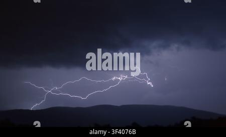 Branching lightning bolt over the Semnoz ridge in a dark storm sky at night, seen from Alby-sur-Chéran, Haute-Savoie, French Alps, France Stock Photo