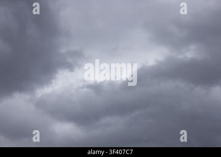 Soft gray storm clouds fill the frame around a pale central opening, creating a cool overcast sky texture with diffused natural light. Broad tonal lay Stock Photo