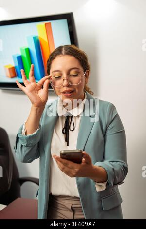 Young businesswoman checking data on her smartphone in a corporate office setting Stock Photo