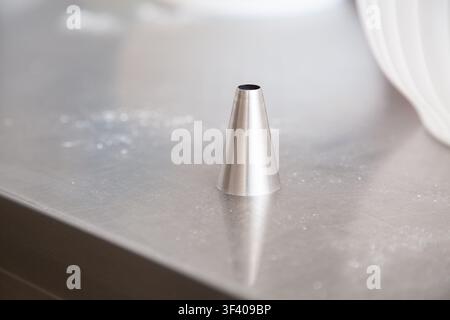 Minimalist stainless steel cone standing on brushed metal surface with soft bright reflections and shallow depth of field, creating clean industrial Stock Photo