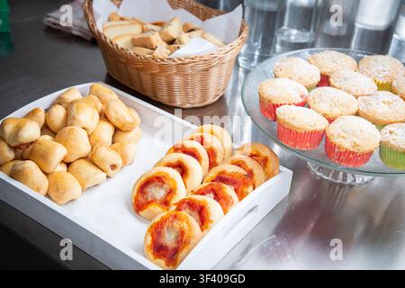 Assorted fresh baked pastries, bread rolls, fruit filled rounds, sugar dusted muffins arranged on serving trays with wicker basket for breakfast Stock Photo