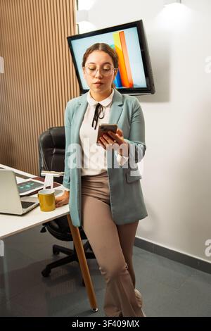 Businesswoman standing in an office reviewing data on a smartphone Stock Photo