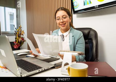 Young woman smiling, analyzing documents and data while working at her office desk Stock Photo