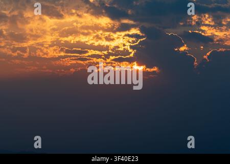 Dramatic sunset with sun partially hidden behind clouds and glowing sky. Stock Photo