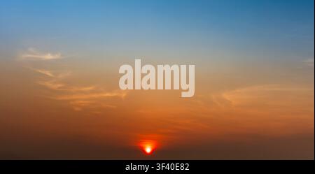 Bright orange sunset with blue gradient sky and soft clouds. Stock Photo