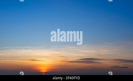 A vivid sunset sky transitions from deep blue to warm orange near the horizon, with wispy clouds Stock Photo