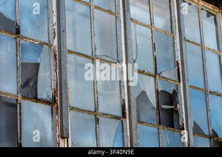 Abstract of broken glass windows in an old industrial building with rusty metal window frames. Stock Photo