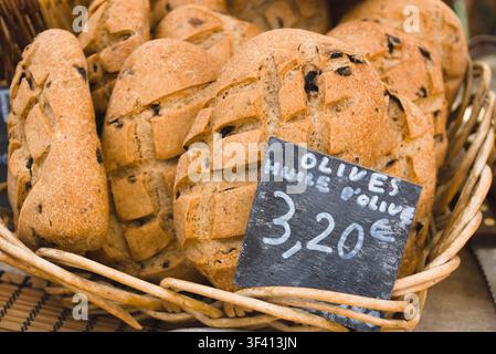 Artisanal olive bread loaves with price tag displayed in a basket at an open-air market in Arles, France. Stock Photo