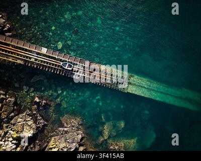 Aerial top down view directly above an old British lifeboat ramp on the Cornish coast sloping down into the sea with a small rowing boat in a Cornwall Stock Photo