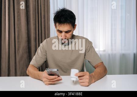Portrait of man connecting smart home device using smartphone, looking at application settings, setting up and controlling smart socket from mobile ap Stock Photo
